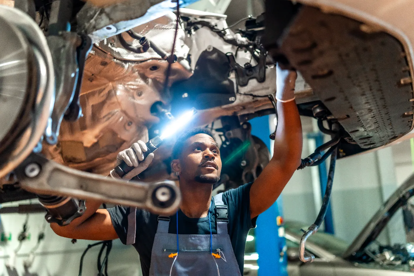 A car mechanic inspecting the vehicle under with flashlight.