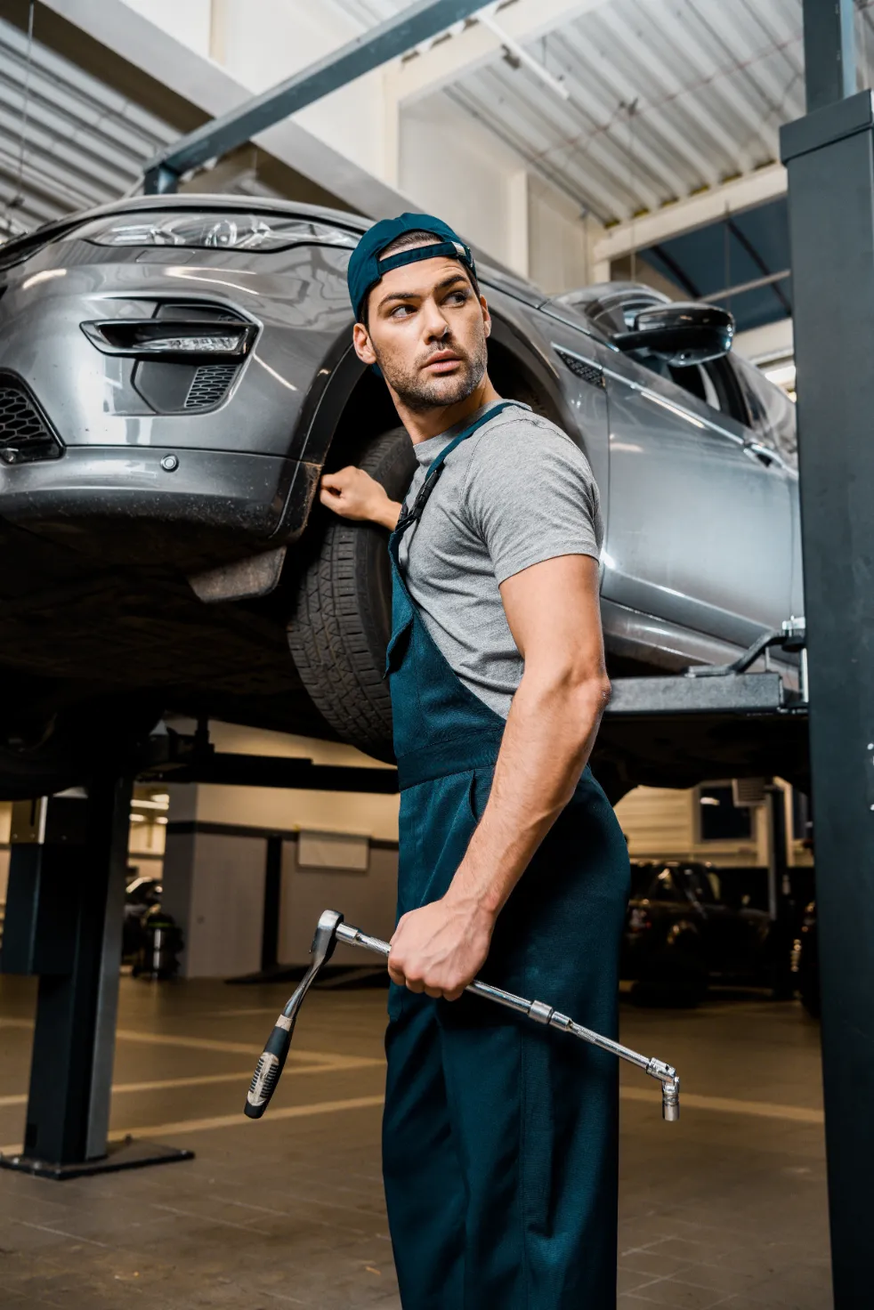 A young auto mechanic holding a wrench while looking away from the car.